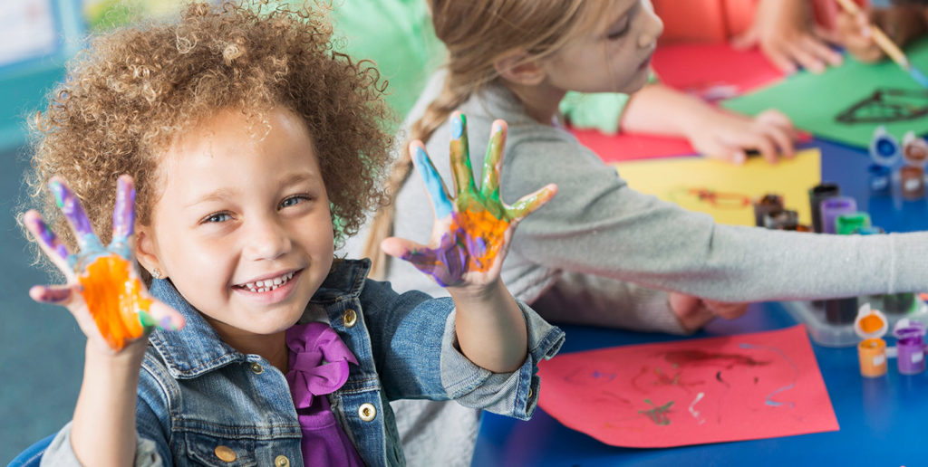 child showing hands covered in colorful paint